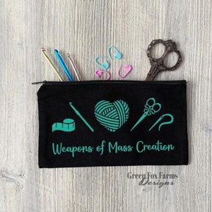 May include: Black zippered pouch with the text "Weapons of Mass Creation" and a green yarn ball, scissors, crochet hook, and measuring tape design. The pouch is made by Green Fox Farms Designs.