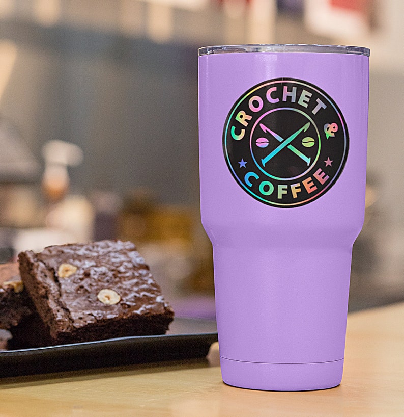 May include: A purple stainless steel tumbler with a black and iridescent sticker that says "Crochet & Coffee" with a crossed crochet hook and coffee bean design.