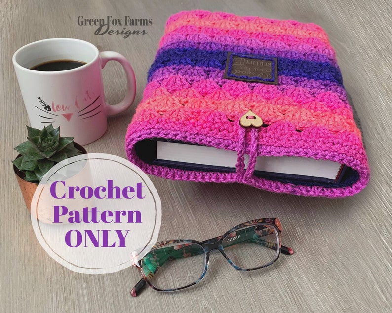 May include: A crochet book cover pattern in pink, purple, and blue with a heart-shaped button. The cover is made with a textured stitch and has a strap to keep it closed. The pattern is available for purchase.
