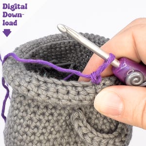 May include: Close-up of a crochet project in progress. A gray crocheted pouch is being worked on with a silver crochet hook and purple yarn. The text "Digital Download" is in the upper left corner.