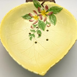 Peut inclure: Un plat en céramique jaune en forme de feuille avec un motif floral en relief et des trous de drainage. Le plat a une poignée en branche brune.