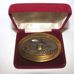 Peut inclure: Boucle de ceinture ovale en bronze de Plow & Planter Works, commémorant leur Centennial Drive de 1919-1984. La boucle est présentée dans un coffret en velours rouge avec une doublure en satin.
