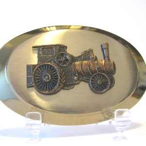 May include: A gold-toned belt buckle with a raised, detailed image of a vintage steam engine in copper tones.