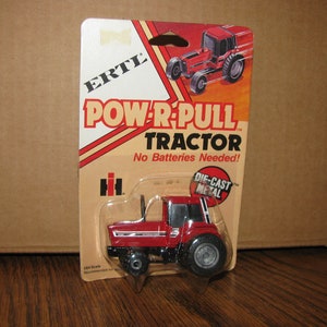 May include: A red die-cast metal toy tractor with the words "POW'R-PULL TRACTOR" and "No Batteries Needed!" on the packaging. The packaging also includes the logo for International Harvester.