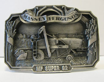 May include: A silver-toned belt buckle featuring a detailed image of a Massey Ferguson Super 92 combine harvester in a field. The buckle has the words "Massey Ferguson" and "MF Super 92" inscribed on it.