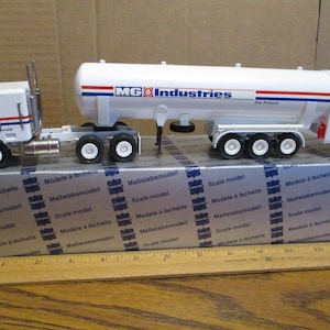 Puede incluir: Modelo blanco de un camión cisterna con un logotipo rojo, blanco y azul que dice "MG Industries". El camión está en una caja blanca con las palabras "Scale model", "Modele a lechelle" y "Maßstabmodell" repetidas en la caja.