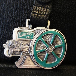 May include: Silver charm of a Galloway engine with a green wheel. The charm has the word "Galloway" printed on it.