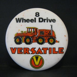 Puede incluir: Un botón blanco con una ilustración de tractor rojo y el texto "8 Wheel Drive VERSATILE" con un logotipo V amarillo.