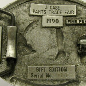 Puede incluir: Una hebilla de cintur&oacute;n de plata con un dise&ntilde;o detallado de un tractor. La hebilla est&aacute; etiquetada con "JI Case Parts Trade Fair 1990 Fine Pewter Gift Edition Serial No. 14".