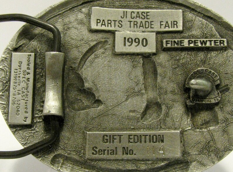 Puede incluir: Una hebilla de cintur&oacute;n de plata con un dise&ntilde;o detallado de un tractor. La hebilla est&aacute; etiquetada con "JI Case Parts Trade Fair 1990 Fine Pewter Gift Edition Serial No. 14".