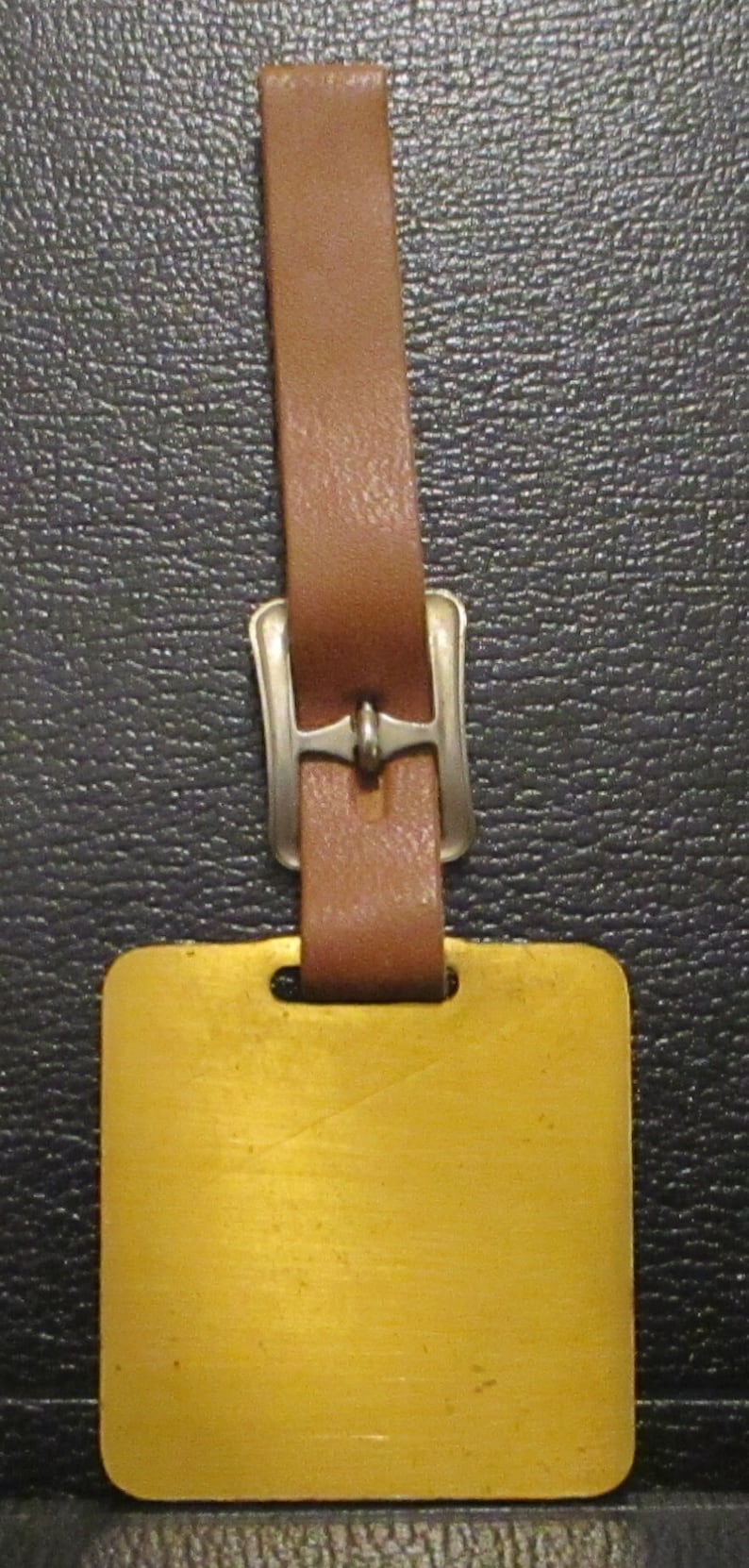 May include: A brown leather luggage tag with a silver buckle and a blank gold metal tag.