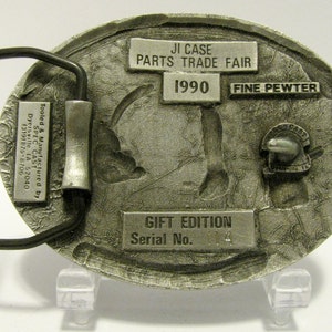 Puede incluir: Una hebilla de cintur&oacute;n plateada con un dise&ntilde;o detallado de un tractor. La hebilla est&aacute; etiquetada con "JI Case Parts Trade Fair 1990 Fine Pewter Gift Edition Serial No. 114".