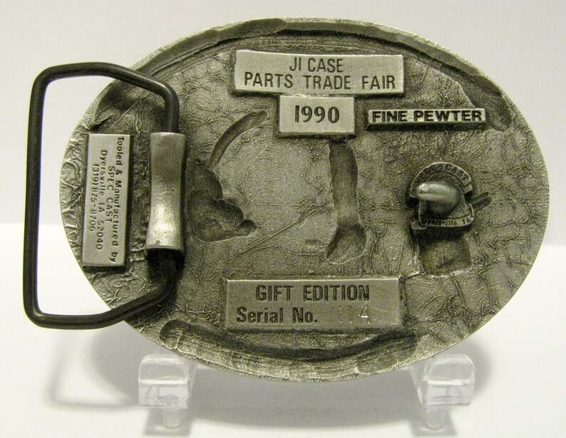 Puede incluir: Una hebilla de cintur&oacute;n plateada con un dise&ntilde;o detallado de un tractor. La hebilla est&aacute; etiquetada con "JI Case Parts Trade Fair 1990 Fine Pewter Gift Edition Serial No. 114".