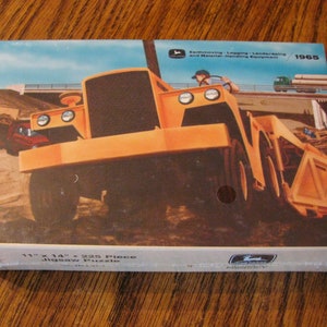 May include: A vintage 1965 John Deere jigsaw puzzle box featuring a yellow tractor with a dump bed. The box is 11 inches by 14 inches and has 225 pieces. The text on the box reads "Earthmoving - Logging - Landscaping and Material-Handling Equipment".