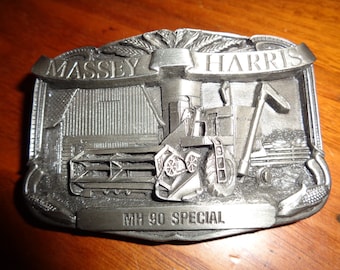 May include: A silver metal belt buckle featuring a detailed image of a Massey Harris MH 90 Special combine harvester. The buckle has a raised inscription "Massey Harris" and "MH 90 Special".