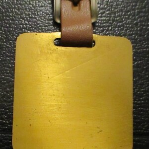May include: A gold-coloured metal luggage tag with a brown leather strap and a silver buckle.