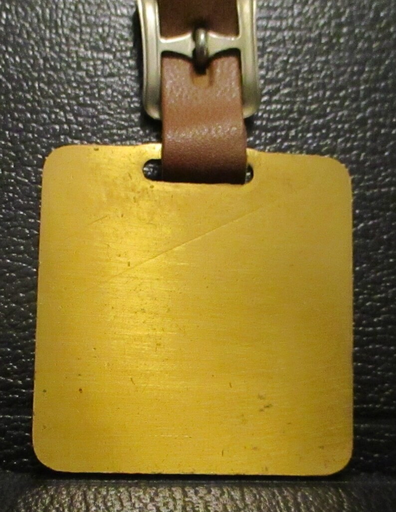 May include: A gold-coloured metal luggage tag with a brown leather strap and a silver buckle.