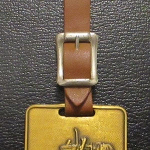 May include: A gold-coloured metal keychain with a brown leather strap and a silver buckle. The keychain features a detailed image of a Komatsu bulldozer with the text "Komatsu" below it.