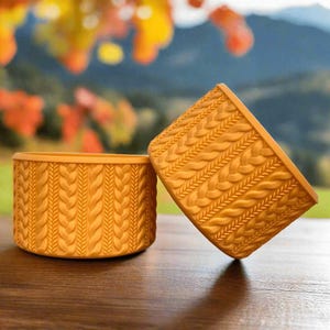 May include: Two yellow ceramic planters with a braided rope design. The planters are on a wooden surface.