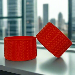 May include: Two orange ceramic planters with a knitted pattern. The planters are round and have a smooth surface.