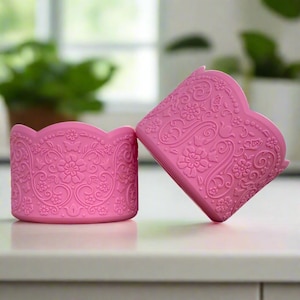 May include: Two pink plastic containers with a decorative floral pattern. The containers are made of a textured plastic and have a scalloped edge.