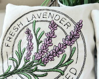 May include: A white fabric pillow with embroidered lavender flowers and the text "Fresh Lavender Hand Picked" in a circle.