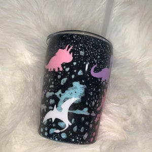 May include: A black tumbler with a splatter paint design featuring pink, purple, and blue dinosaur silhouettes.