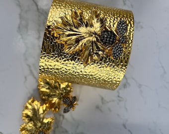 May include: A gold-toned cuff bracelet and matching earrings feature a leaf design with a bee accent. The bee is adorned with black rhinestones.