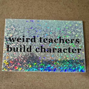 May include: Rectangular plaque with a glittery, iridescent surface. The text "weird teachers build character" is printed in black. The glitter includes silver, blue, green, pink, and yellow colors.
