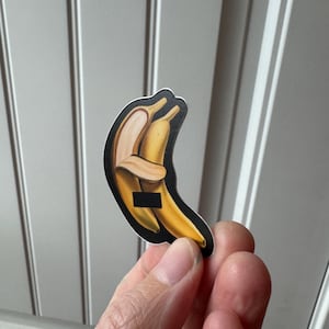 May include: A sticker featuring two yellow bananas embracing, one partially peeled. The sticker has a black border and a small black rectangle obscuring a portion of the image. The design is a playful illustration.