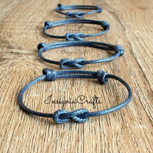 May include: Four grey infinity knot bracelets made of cord. The bracelets are stacked on top of each other on a wooden surface. The text "Insignia Crafts" is visible on the bottom bracelet.