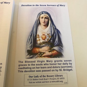 May include: A religious card with a picture of the Virgin Mary with seven swords piercing her heart. The text reads "Devotion to the Seven Sorrows of Mary" and "The Blessed Virgin Mary grants seven graces to the souls who honor her daily by meditating on her tears and dolors (sorrows). This devotion was passed on by St. Bridget." The card also includes the name and address of "Our Lady of the Rosary Library".