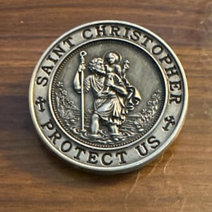 May include: A silver-colored Saint Christopher medal. The medal features an image of Saint Christopher carrying a child across water, surrounded by the words "SAINT CHRISTOPHER PROTECT US".