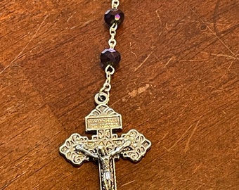 May include: A silver rosary with a crucifix and dark purple glass beads.
