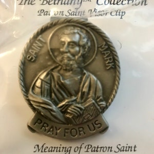 May include: Silver-toned metal visor clip featuring Saint Mark with the words "Saint Mark" and "Pray for Us". The Bethany Collection Patron Saint Visor Clip.