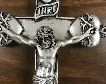 May include: Silver-toned metal crucifix with a figure of Jesus Christ on the cross. The cross has two hearts with thorns at the top and bottom, and a banner with the inscription "INRI".