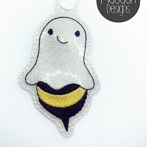 May include: A white glitter ghost with a black outline and a yellow and black bee body. The ghost has a smiling face with black eyes. The keychain is attached to a silver ring.