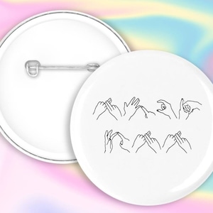 May include: White button with a black outline of hands signing the word "love" in American Sign Language.