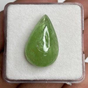 Puede incluir: Una gema verde claro en forma de pera, exhibida en una caja de pl&aacute;stico transparente con un interior blanco texturizado. La gema pulida tiene una superficie lisa y un aspecto transl&uacute;cido, mostrando su color natural y caracter&iacute;sticas internas.