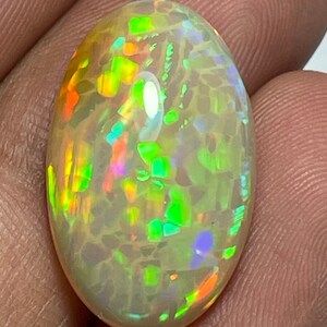 May include: Oval-shaped opal gemstone with a creamy white base color. The opal displays vibrant flashes of color, including green, orange, and blue, creating a play-of-color effect. The gemstone is polished and smooth.