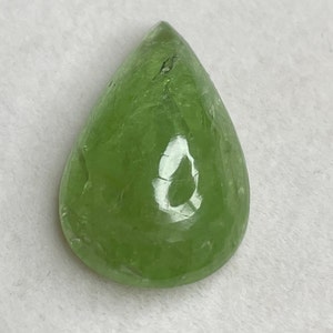 Puede incluir: Una gema transl&uacute;cida en forma de pera, de color verde claro. La superficie pulida refleja la luz, mostrando patrones internos y ligeras imperfecciones. La forma es alargada, con una base redondeada y una parte superior puntiaguda, adecuada para joyer&iacute;a.