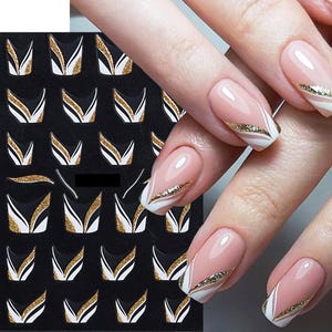 May include: A sheet of black nail stickers with white and gold geometric designs. The stickers are arranged in rows and columns. The sheet is shown with a hand wearing the stickers on the nails.
