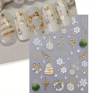 May include: White nail art with gold Christmas tree, star, and bow designs. The image also shows a sheet of nail art stickers with gold and white Christmas-themed decorations, including snowflakes, ornaments, and wreaths.