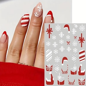 May include: Christmas-themed nail art featuring red and white designs. The nails showcase a variety of festive patterns, including candy cane stripes, snowflakes, and Santa hats. A sheet of matching nail decals is also visible.