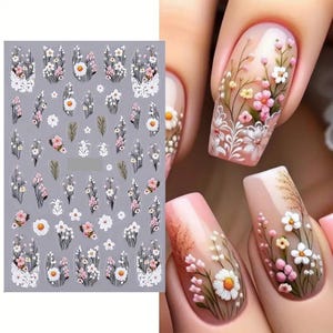 May include: A sheet of nail stickers with a variety of white and pink floral designs. The stickers feature small flowers, leaves, and stems.