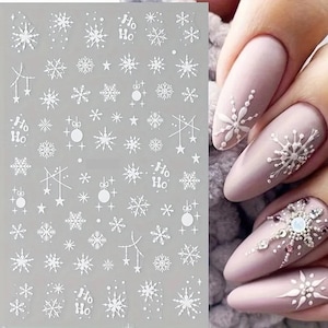 May include: White nail art stickers featuring various snowflake designs, stars, and the text "Ho Ho". The stickers are on a clear sheet, with examples of snowflake nail art on painted nails.