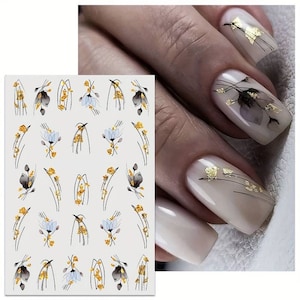 Può includere: Sticker per nail art con un design floreale con accenti neri, bianchi e dorati. Gli sticker sono disposti in file su un foglio bianco.