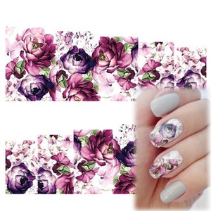 Può includere: Sticker per nail art con un design floreale con fiori viola e rosa su sfondo bianco. Gli sticker sono mostrati applicati alle unghie.