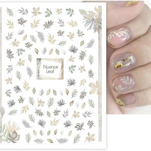 Könnte beinhalten: Ein Bogen mit Nagelkunst-Aufklebern mit verschiedenen Blattdesigns in Grün-, Grau- und Goldtönen. Der Bogen enthält den Text "Nuance Leaf". Das Bild zeigt auch eine Hand mit manikürten Nägeln, einige mit Blattdesigns und goldenen Akzenten.