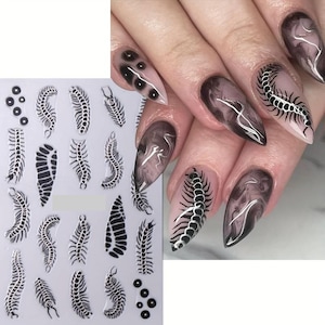 Könnte beinhalten: Schwarz-weiße Nagelkunst-Aufkleber mit Tausendfüßler- und Segmentmustern. Das Bild zeigt auch lange, spitze Nägel mit einem dunklen, rauchigen Effekt und Tausendfüßler-Nagelkunst.